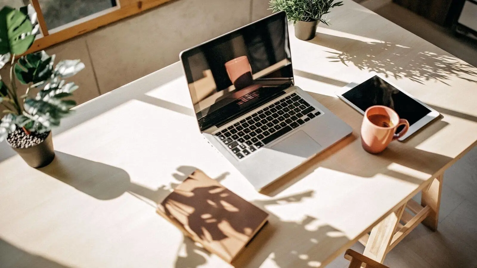 Auf dem Tisch steht ein Laptop, iPad und eine Tasse.