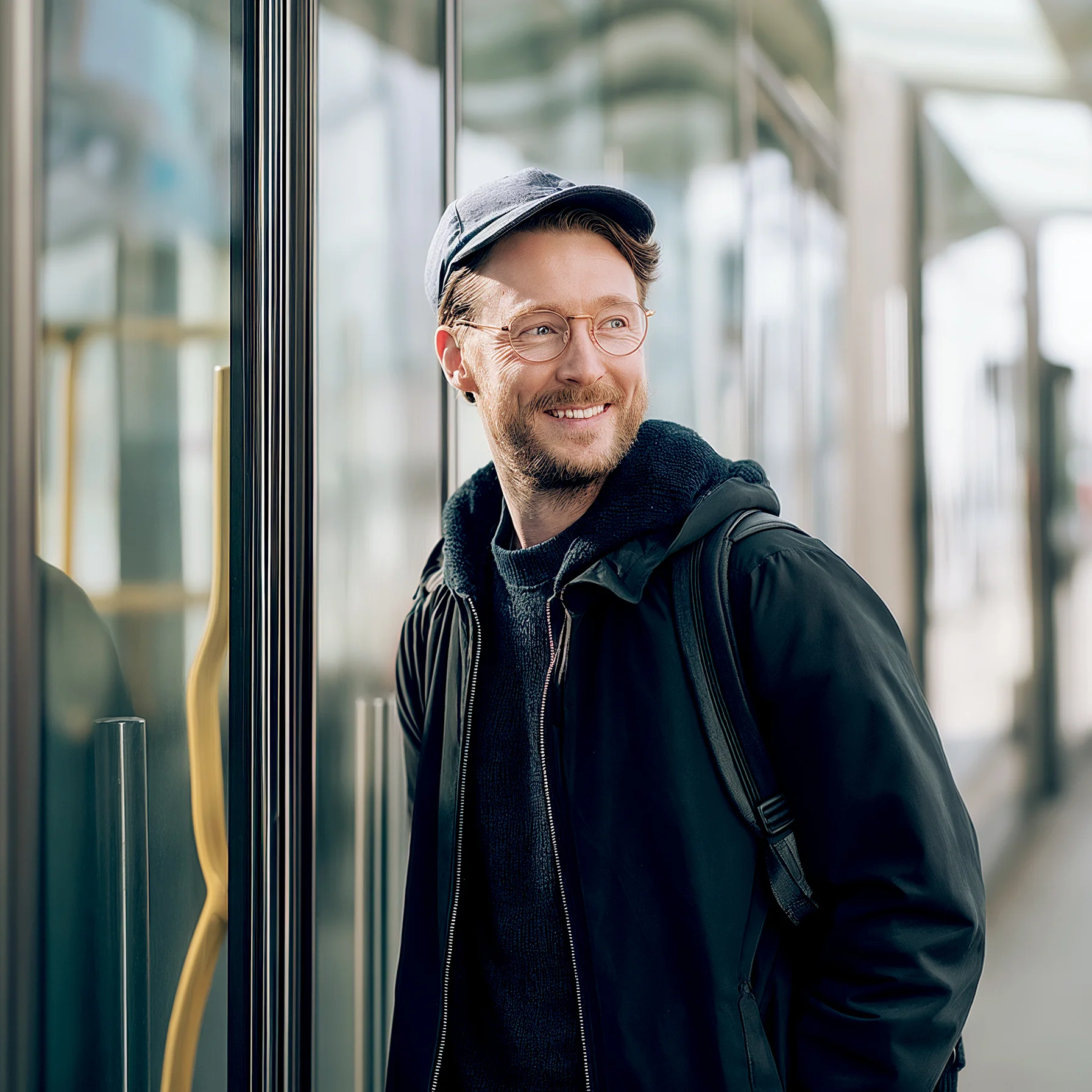 Mann steht am Bahnhof vor einem Zug und lächelt.