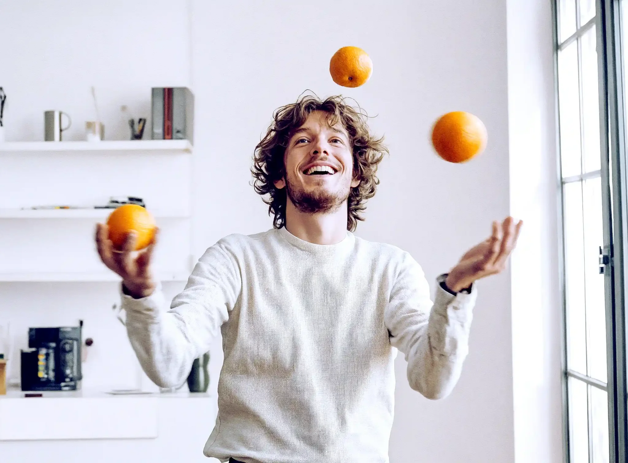 Mann jongliert mit Orangen und lacht nebenbei.
