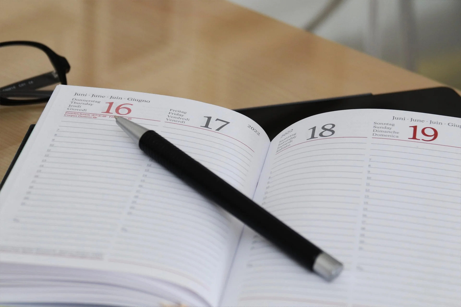 Aufgeschlagener Kalender mit den Juni-Daten 16 bis 19; ein Stift liegt quer über den Seiten, eine Brille liegt im Hintergrund.