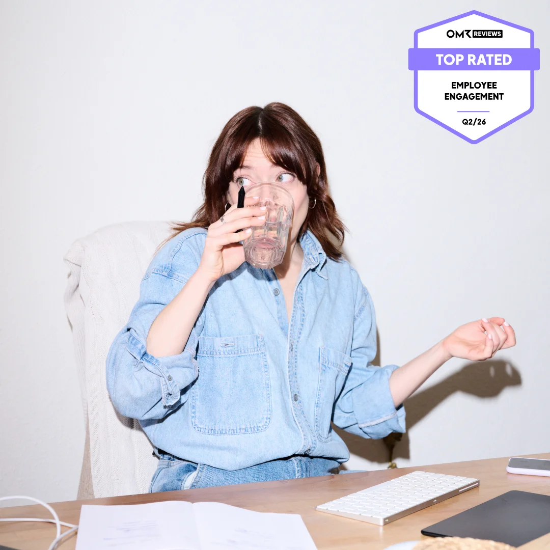 Person sitzt am Schreibtisch, trinkt aus einem Glas und schaut überrascht zur Seite; im Bild ist ein „Top Rated Employee Engagement“-Badge von OMR Reviews (Q2/26) eingeblendet.