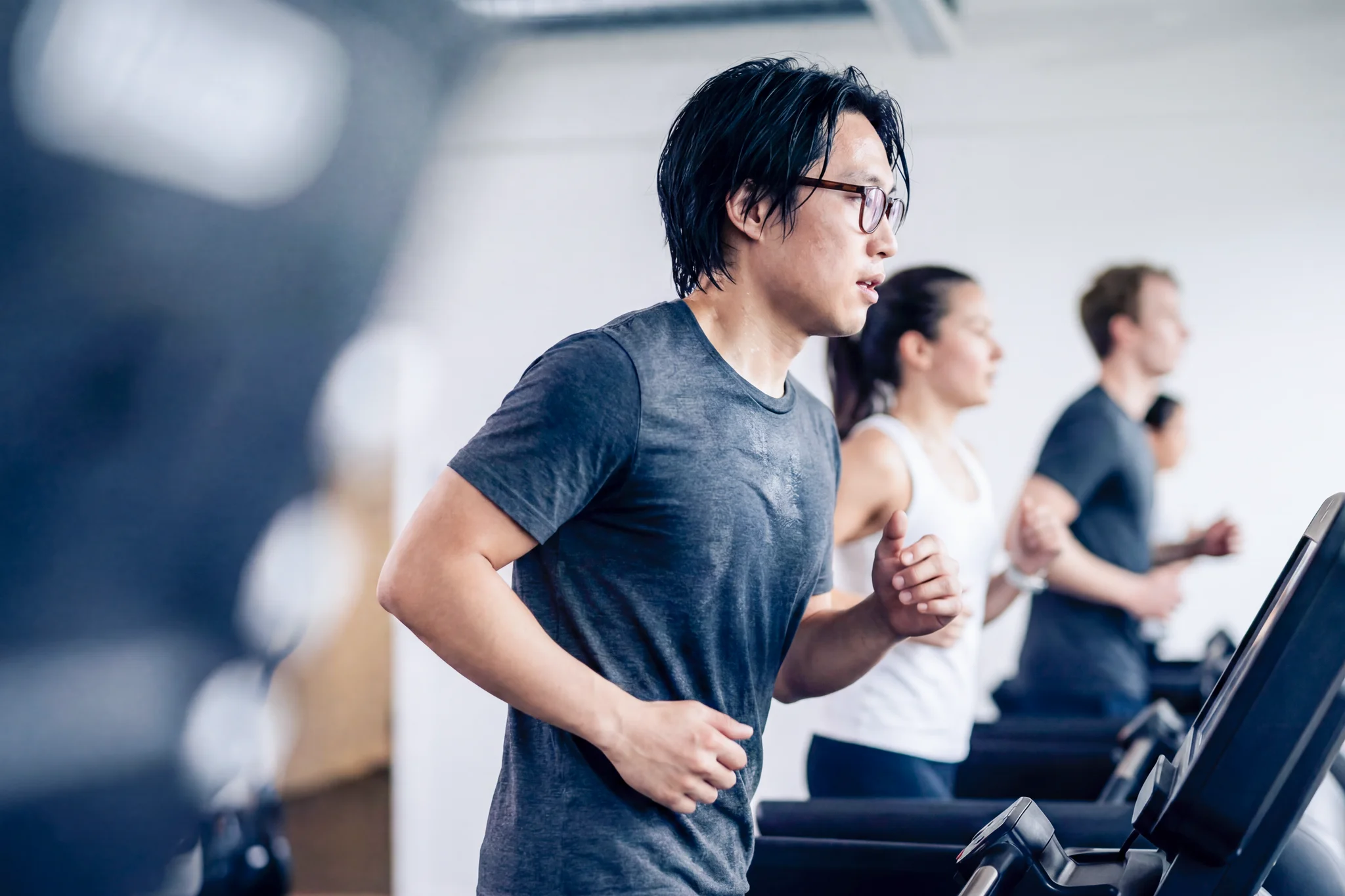 Mann joggt auf einem Laufband im Fitnessstudio; im Hintergrund trainieren weitere Personen.