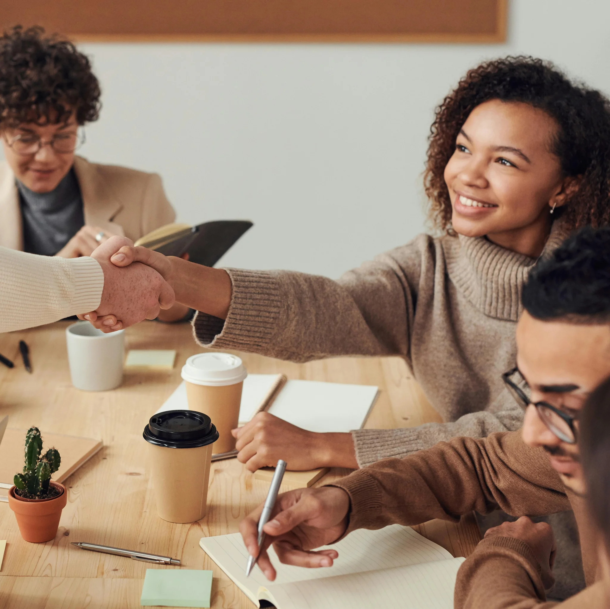 Sachbezug Minijob Menschen sitzen an einem Tisch. Zwei Personen geben sich die Hand.