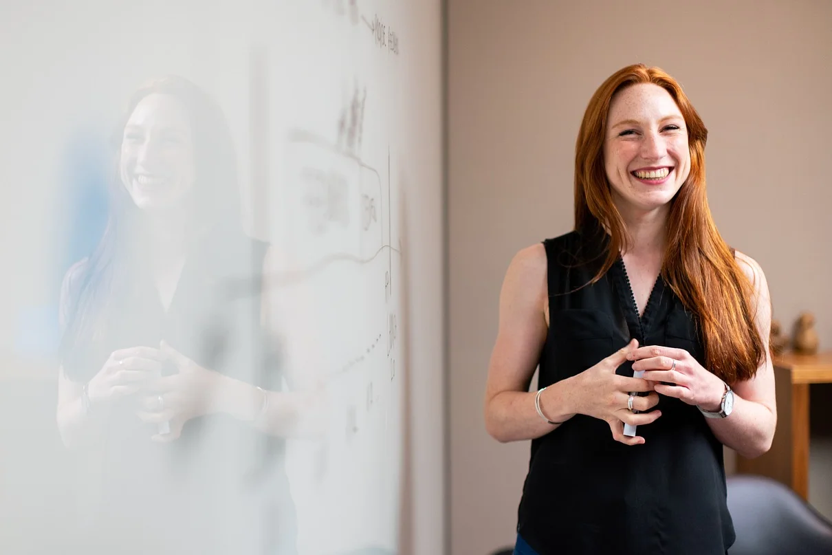 Frau steht Lächelnd neben einem Whiteboard.