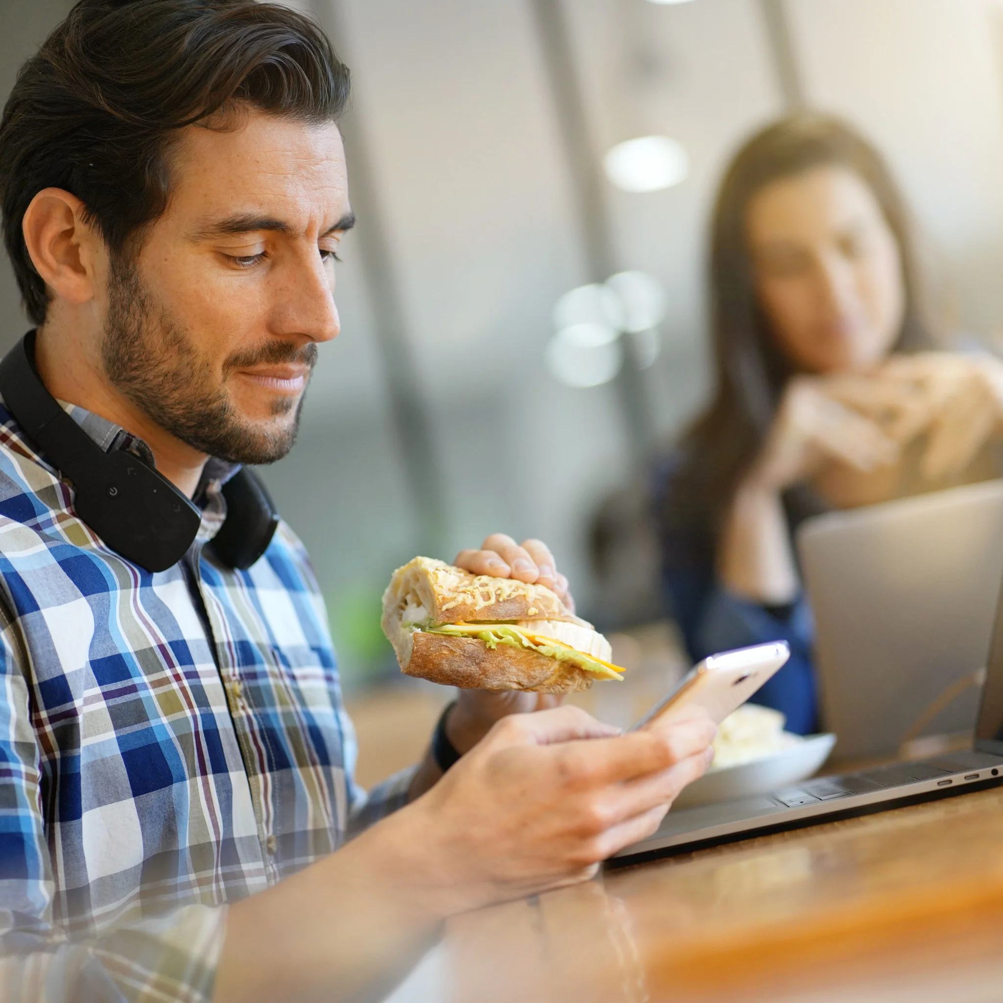 Mann schaut auf Smartphone und isst Sandwich