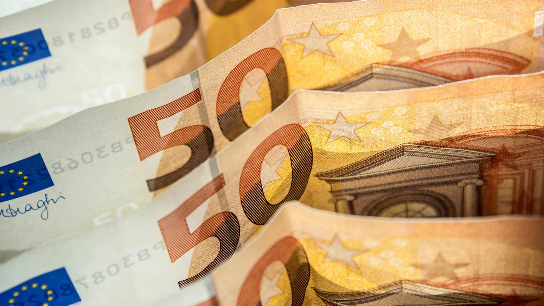 Vor- und Nachteile von Bonuszahlungen Mehrere 50-Euro-Banknoten liegen leicht versetzt übereinander. Die Abbildung zeigt Details der Euro-Scheine mit Wertangabe, Sternen und architektonischen Motiven.