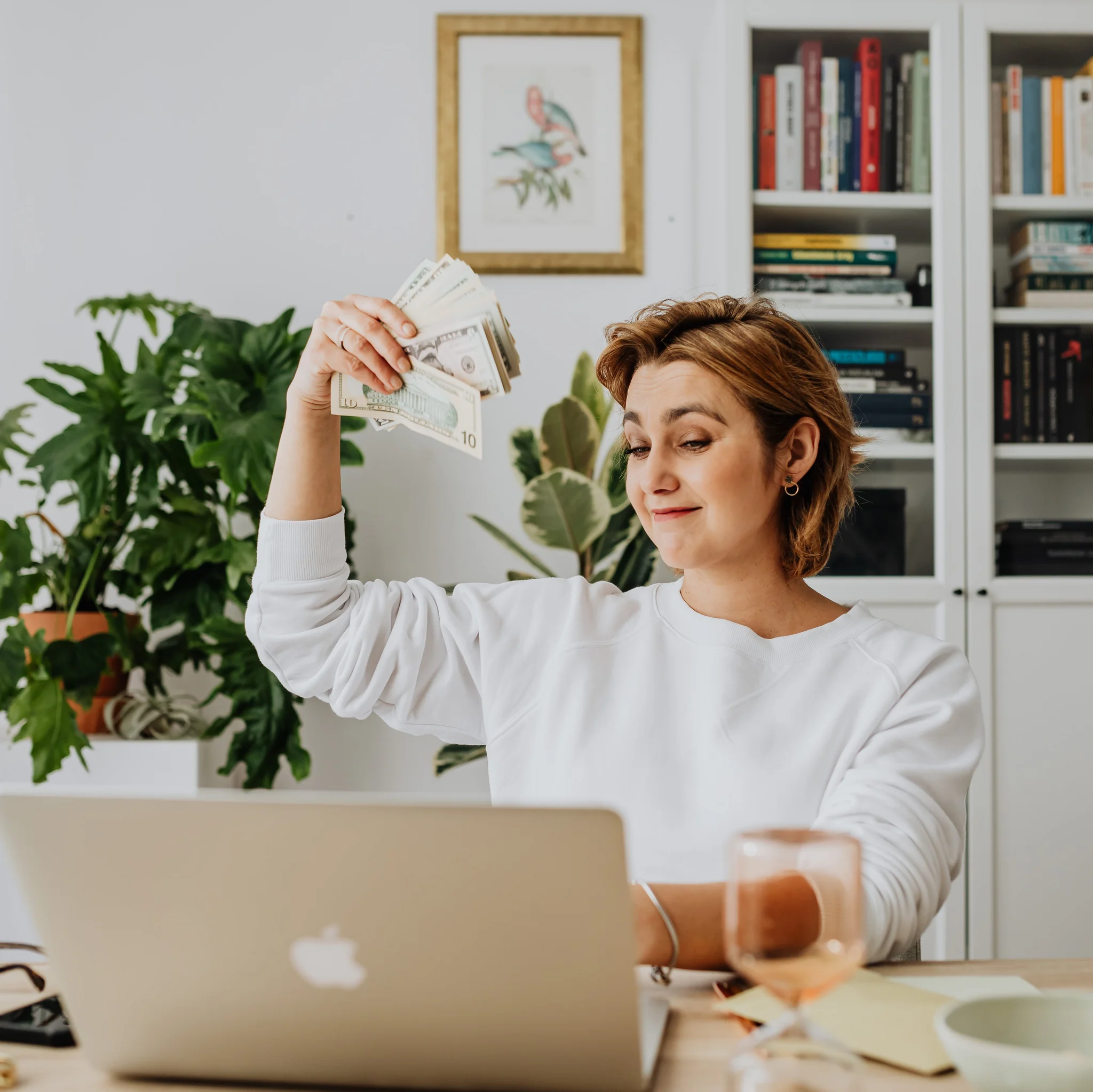 Bonussystem für Mitarbeiter Frau sitzt vor Laptop um hält aufgefächertes Geld in der Hand.