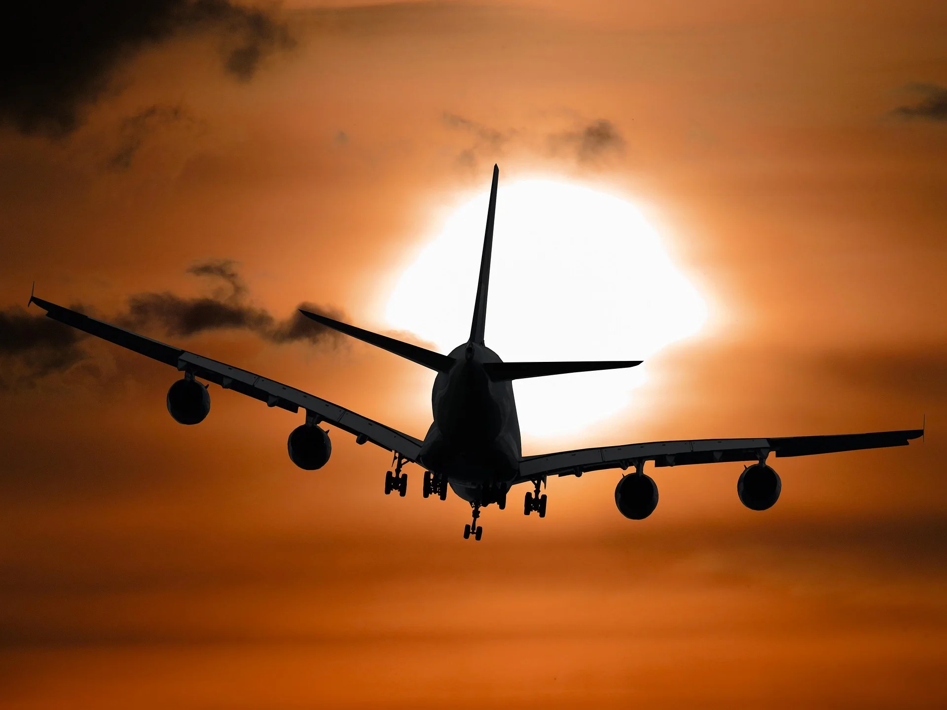 Silhouette eines großen Passagierflugzeugs im Landeanflug vor einer tief stehenden Sonne und orangefarbenem Himmel.