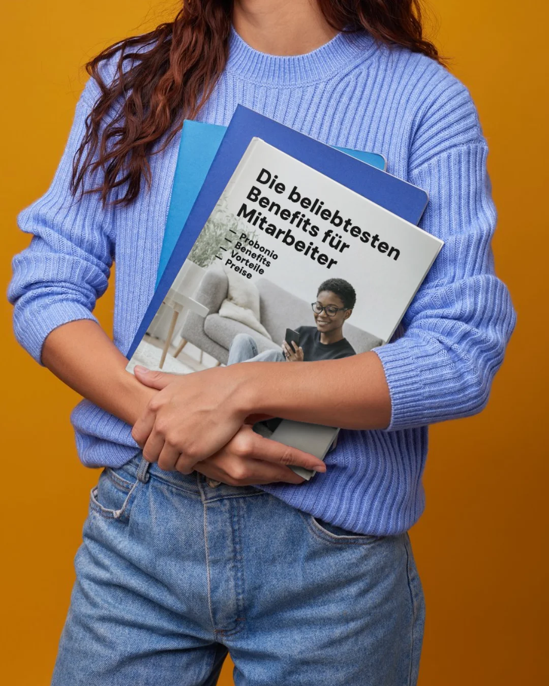 Person in blauem Pullover hält eine Broschüre mit dem Titel „Die beliebtesten Benefits für Mitarbeiter“ vor gelbem Hintergrund.
